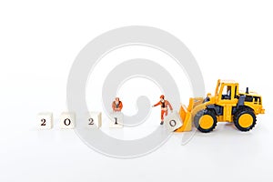 Miniature worker moving wooden cube with yellow front end loader truck