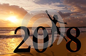 Happy new year card 2018. Silhouette young woman jumping on tropical beach over the sea and 2018 number with sunset background