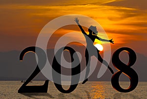 Happy new year card 2018. Silhouette young woman jumping on tropical beach over the sea and 2018 number with sunset background