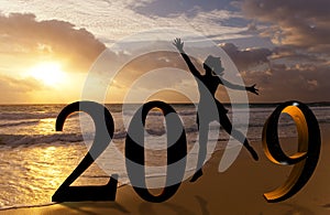 Happy new year card 2019. Silhouette young woman jumping on tropical beach over the sea and 2019 number with sunset background
