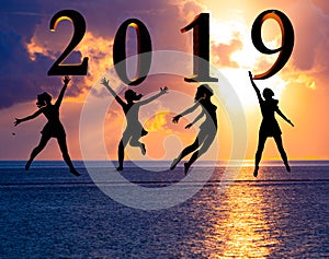 Happy new year card 2019. Silhouette young woman jumping on tropical beach over the sea and 2019 number with sunset background