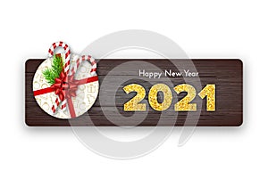 Happy New Year card 2021. Holiday gift with fir tree branches, candy canes and red bow on wood background. Celebration