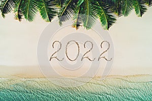 Happy new year concept, 2022 written on the sand. Summer holiday on tropical island. Palm trees and sea waves