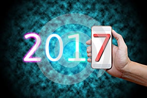 2017 Happy New Year Concept, Body part, Hand holding mobile phone and number seven on screen.