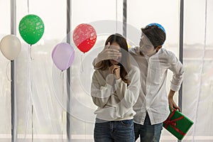 Happy New Year and couple concept. Asian young man surprise and close woman eye by right hand and holding green gift box behide