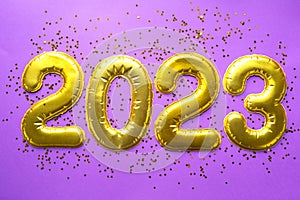 Happy New Year- golden numbers 2023 on a purple background with sequins, stars, glitter, lights of garlands. Greetings, postcard.