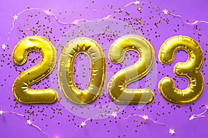 Happy New Year- golden numbers 2023 on a purple background with sequins, stars, glitter, lights of garlands. Greetings, postcard.
