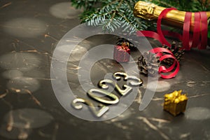 Happy new year 2023 greeting card on a brutal metal background with a branch of a Christmas tree, bright lights and a bottle of