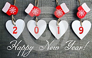 Happy New Year greeting card.Decorative white wooden Christmas hearts and red mittens with 2019 numbers on old wooden background.