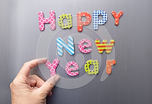Happy new year, hand making message from magnetic letters on fridge
