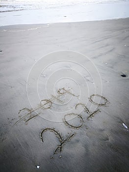 Happy new year 2020, lettering on the beach with wave and clear blue sea. Numbers 2020 year on the sea shore.