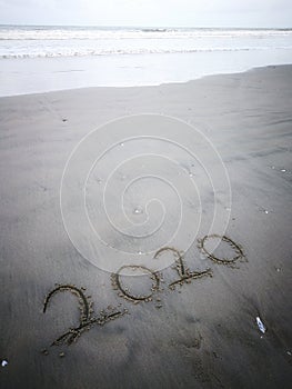 Happy new year 2020, lettering on the beach with wave and clear blue sea. Numbers 2020 year on the sea shore.