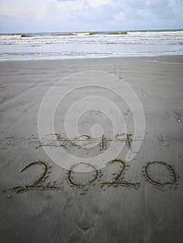 Happy new year 2020, lettering on the beach with wave and clear blue sea. Numbers 2020 year on the sea shore.