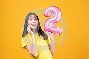 Happy new year and Merry Christmas concept. Beautiful young asian woman with balloons number 2 on yellow background