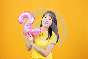 Happy new year and Merry Christmas concept. Beautiful young asian woman with balloons number 2 on yellow background