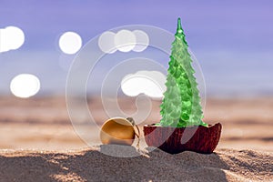 Happy New Year and Merry Christmas greeting card. Christmas tree and ball on beach and sea with bokeh in background