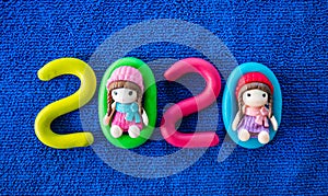 Happy New Year 2020 , molding of color clay with little girls toys on blue background.