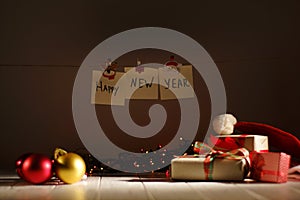 The Happy New Year sign is hanging on the rope with the help of Christmas foldings behind the presents, glowing garlands