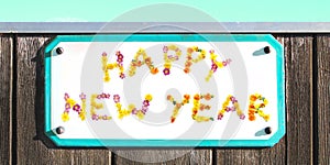 HAPPY NEW YEAR sign of yellow pink red and orange flowers collage, wooden wall. aquamarine sign, frame, turquoise sky