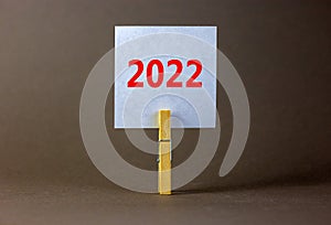 2022 happy new year symbol. Wooden clothespin, white sheet of paper with number 2022. Beautiful grey background, copy space.