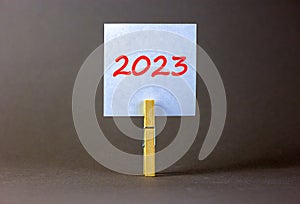 2023 happy new year symbol. Wooden clothespin, white sheet of paper with number 2023. Beautiful grey table grey background, copy