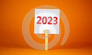 2023 happy new year symbol. Wooden clothespin, white sheet of paper with number 2023. Beautiful orange table orange background,