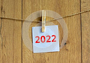 2022 happy new year symbol. Wooden clothespin, white sheet of paper with number 2022. Beautiful wooden background, copy space.