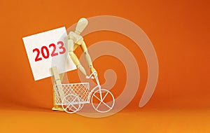 2023 happy new year symbol. Wooden clothespin, white sheet of paper with number 2023. Miniature bicycle model. Beautiful orange