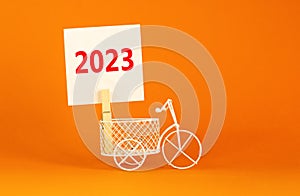 2023 happy new year symbol. Wooden clothespin, white sheet of paper with number 2023. Miniature bicycle model. Beautiful orange