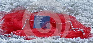 Happy New Year text on black card with red tulle and beads on white fluffy background