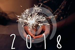 Happy new year text 2018. hand holding a burning sparkler firew