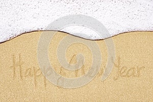 Happy new year written in sand on beach.