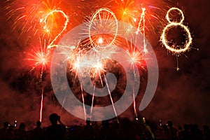 Happy new year 2018 written with sparklers and colorful fireworks as a background. Celebrating party people.