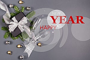 Black handmade gift boxes decorated with silver ribbon, tree branches, two glasses champagne confetti on gray background.