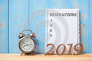 2019 Happy New years with Resolution text on notebook, retro alarm clock and wooden number on table and copy space