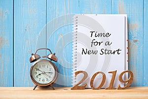 2019 Happy New years with Time for a New Start text on notebook, retro alarm clock and wooden number on table and copy space.