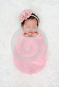 Happy newborn baby girl sleeping in cloth wrap blanket on bed