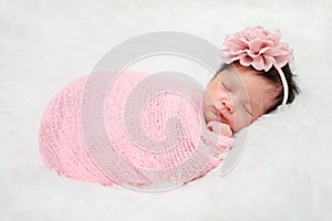 Happy newborn baby girl sleeping in cloth wrap blanket on bed