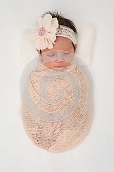 Happy newborn baby girl sleeping in cloth wrap blanket on bed