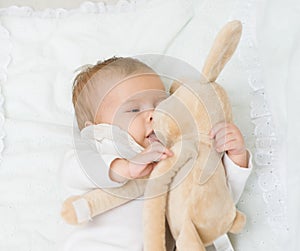 Happy newborn baby plays with toy rabbit