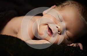 Happy newborn baby smiling in his sleep on a dark