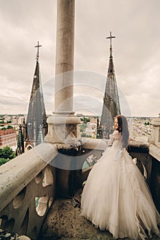 Happy newlywed. beautiful bride in long luxury white dress on the balcony of old gothic cathedral with panoramic city views