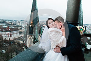 Happy newlywed bride and groom have a sweet ardent moment on the balcony of old gothic cathedral