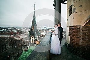 Happy newlywed bride and groom holding each other on the balcony of old gothic cathedral
