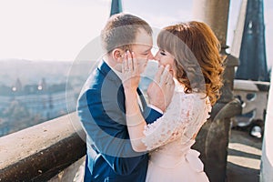 Happy newlywed bride and groom kissing on the balcony of old gothic cathedral