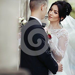 Happy newlywed brunette bride hugging handsome groom near old wa