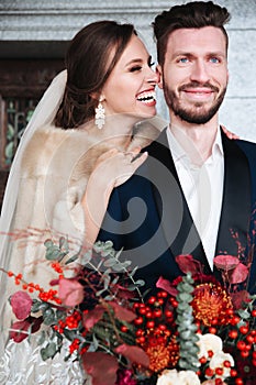 Happy newlywed couple posing and smiling in wedding dress and suit with flowers