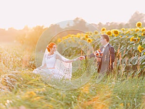 Happy newlywed couple at their wedding day in the sunflower field on sunset.