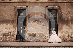 Happy newlywed couple on a walk in old European town street, gorgeous bride in white wedding dress together with handsome groom