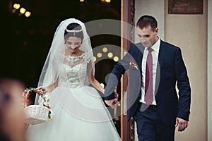 Happy newlywed romantic couple coming out of church after wedding ceremony with a candy basket